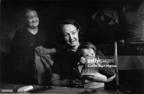 Child sits on her mother's lap to drink, in a poor area of Wigan in northern England. Original Publication: Picture Post - 228 - Wigan - pub. 1939