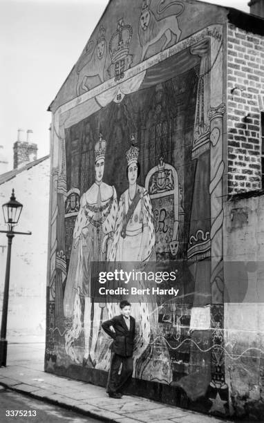 Young boy stands by a mural of Queen Elizabeth II and Prince Philip in Belfast. Original Publication: Picture Post - 7825 - Belfast - pub. 1955