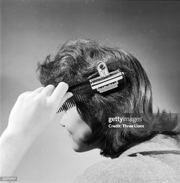 Woman using a handmade hair trimmer, made from a razor blade, a comb and a clip.