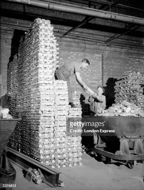 Two men stacking ingots of recycled aluminium in a wharehouse. The aluminium has been recycled from pots and pans.