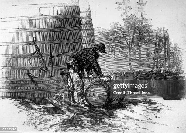 Man filling barrels with oil from a large wooden tank on site at an oil-field.