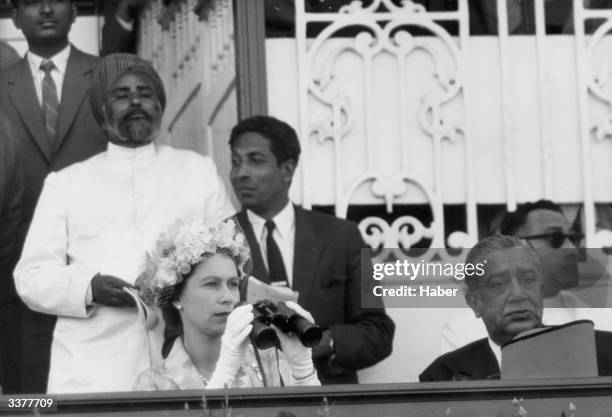 Queen Elizabeth II watching a race through binoculars from a grandstand at the Calcutta races during a State Visit to India with The Prince Philip,...