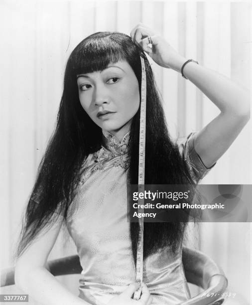 American-Chinese actress Anna May Wong measuring the length of her hair.