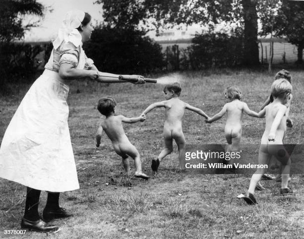 Children at the Coaxden Babies Home playing with a nurse who chases them with a water sprayer on a hot summer afternoon.