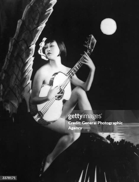 American-Chinese actress Anna May Wong playing a guitar.