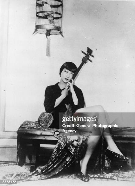American-Chinese actress Anna May Wong sitting holding a string instrument.