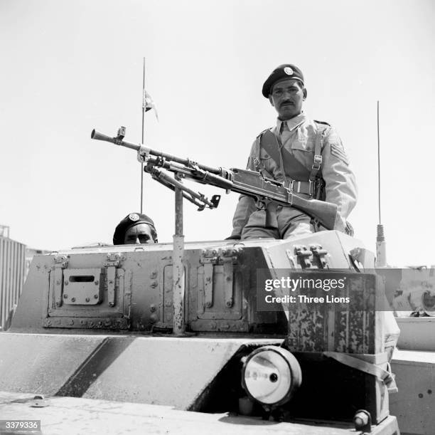 Member of the crack Jordanese regiment the Arab Legion, sitting behind a machine gun fixed to an armoured car.