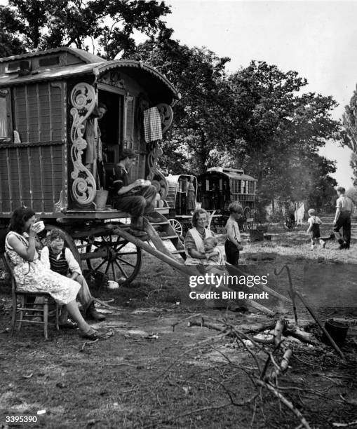 Family of gypsies sitting outside their caravan on an encampment at Brook Farm during the fruit picking season. Original Publication: Picture Post -...