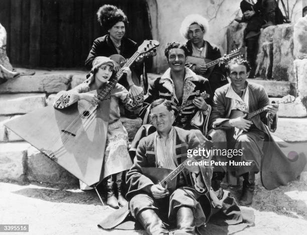 Actors John Gilbert and Renee Adoree pose with a troupe of Russian musicians during the filming of the MGM production 'The Cossacks'. Renee is...