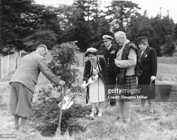 Queen Elizabeth planting a tree in the grounds of Brodick Castle on the Isle of Arran while King George VI and the Duke of Montrose look on. Arran,...