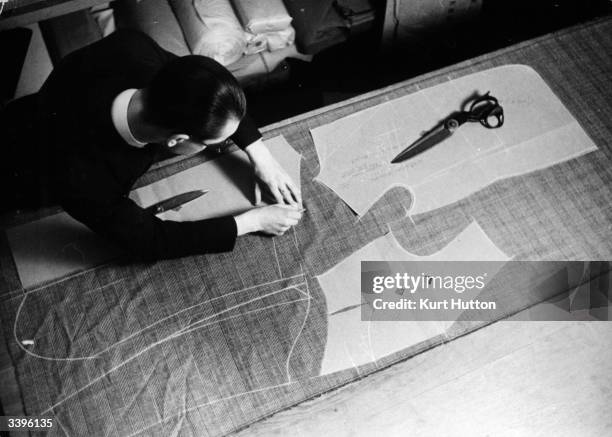 Savile Row tailor using a stiff cardboard pattern to cut out the pieces of material needed to make the sections of a suit. Original Publication:...