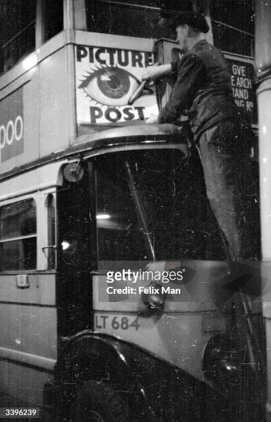 Bill poster balances on a ladder as he pastes an advertisement for Picture Post on the front of a London double decker bus. Original Publication:...