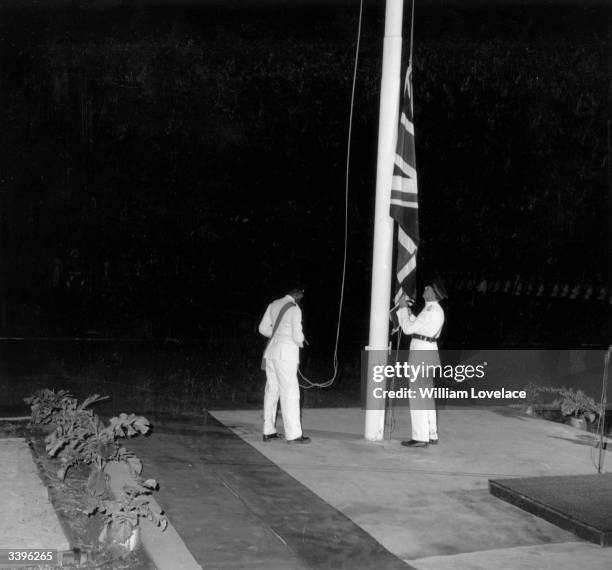 Military officers in ceremonial dress lowering the Union flag at the Jamaican Independence day ceremony.