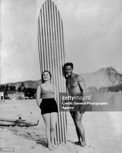 Couple with a large striped surfboard. The man is Olympic swimming champion and pioneer surfer Duke Kahanamoku , a Hawaiian hero.