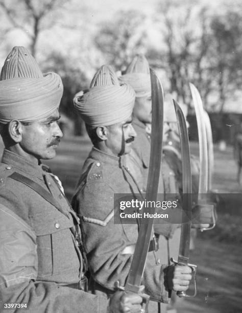 Soldiers of the Indian Mule Contingent standing in line holding swords upright during training in the West of England.