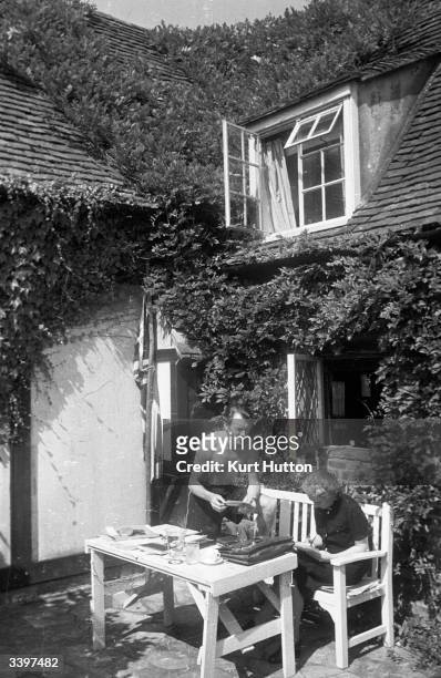 English actor John Mills dictating a letter to his wife playwright Mary Hayley-Bell in the garden of their cottage in Denham village, England....