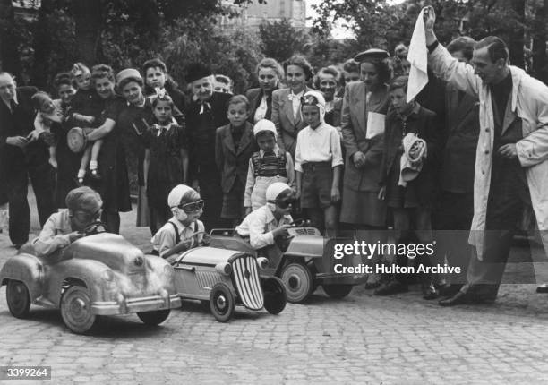 Children's pedal car race set in Berlin zoo being started by German film star Erich Fiedler. Friends and family offer support.