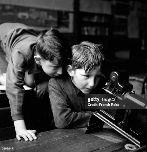 Two boys examining the film projector that their class uses, looking inside to see how it works. Original Publication: Picture Post - 4564 - The...