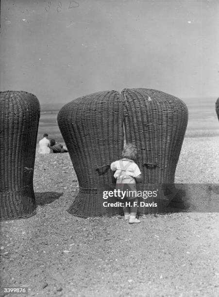 Curious toddler tries to get between two wicker deckchairs on the beach at Rhyl, north Wales.