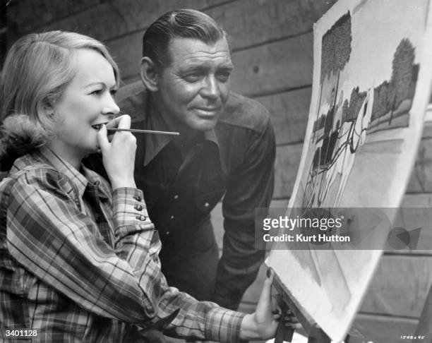 American actor Clark Gable admires his wife Sylvia Ashley's painting of the two of them in a pony cart, during location filming of the MGM production...