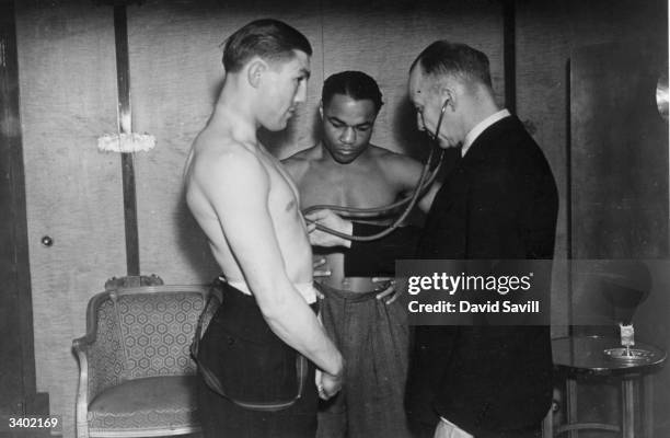 Doctor listens to Liverpool middleweight boxer Ernie Roderick's heart while his opponent Hurrican Henry Armstrong looks on. He lost on a points...