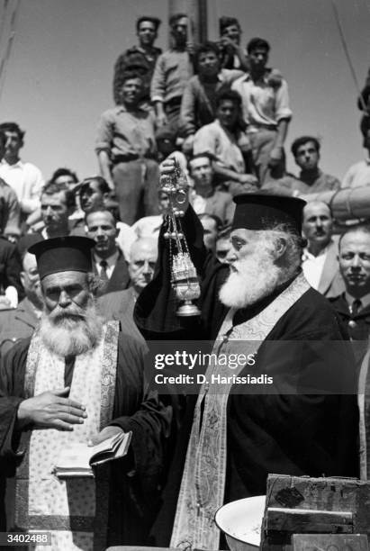 Priest swinging a censer blesses a caique and its crew before it departures with the rest of the sponge fishing fleet from the island of Kalymnos in...