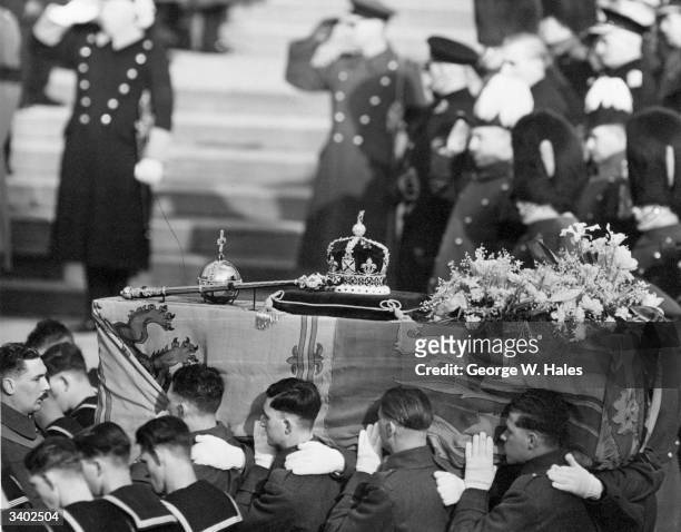 The coffin of George VI, draped with the royal standard being carried by soldiers at his funeral, 15th February 1952. On the top are symbols of...
