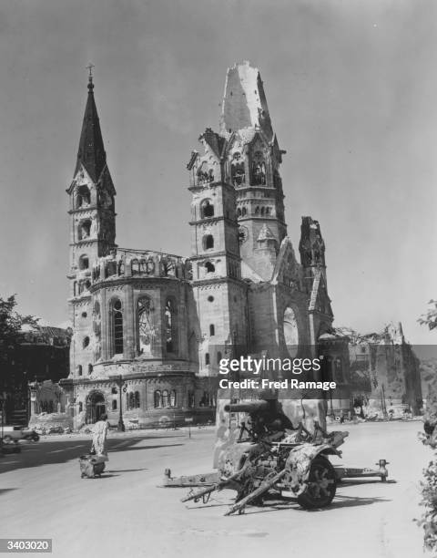 Berlin housewife pulls her belongings behind her past the ruins of a German gun emplacement and the Kaiser Wilhelm Memorial Church, after the Allied...