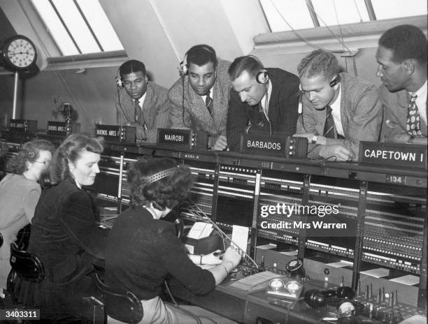 West Indies cricketers watch a telephone operator putting calls through to the West Indies for them from the International Exchange in the City of...