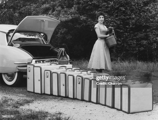 Italian film actress Gina Lollobrigida standing beside a row of suitcases which amazingly all fit into the boot of a Citroen DS 19.