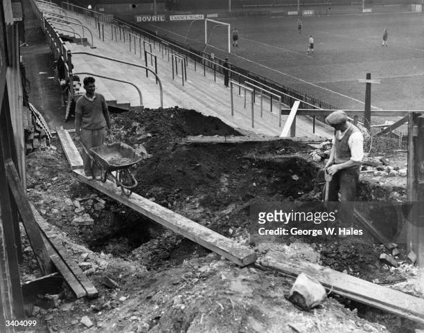 Players train on the pitch as builders get to work on the new stand at Brentford Football Club's Griffin Park stadium, in West London.