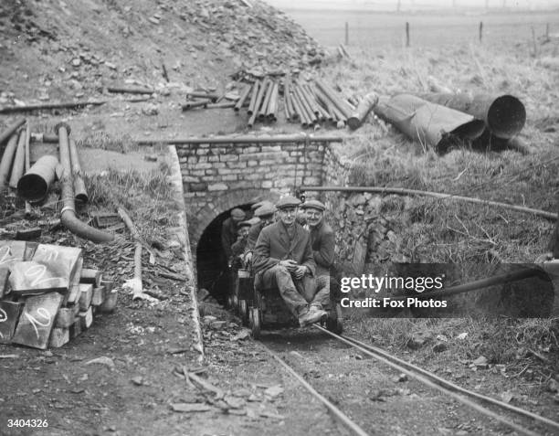 Miners emrge back into the light from a coal mine on a miniature railway carriage.