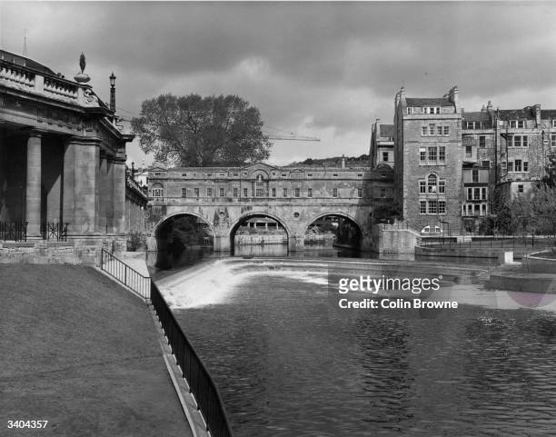 The recently completed weir on the river Avon at Bath, near the famous Pulteney Bridge, with its arcade of shops over the river.