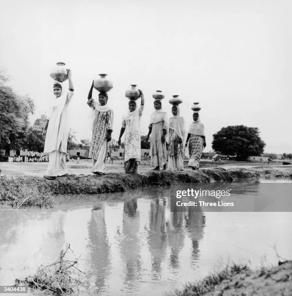 Women carrying copper water jars on their heads walk beside an irrigation canal in Maryabad a Christian village some 60 miles from Lahore.