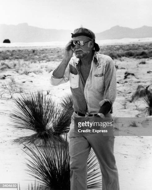 American film director Sam Peckinpah walking across a salt marsh in sweltering heat.