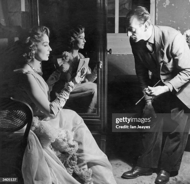 British actress Valerie Hobson wearing a dress by designer Sophie Harris and being tended to by make-up artist Paul Rabiger during the production of...