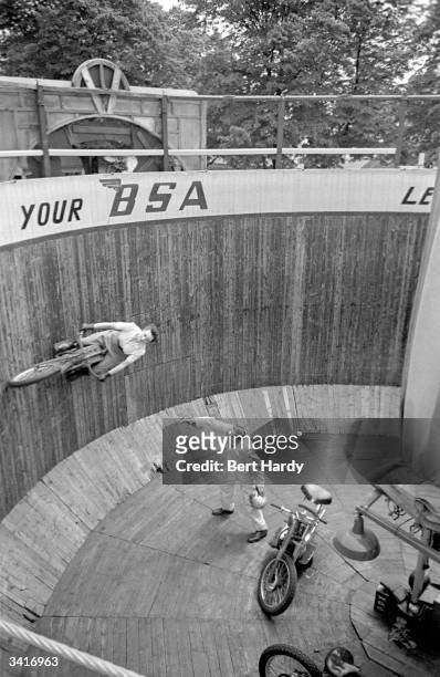 Maureen Swift practising on the wall of death while her partner, Tornado Smith, looks on. Original Publication: Picture Post - 4808 - Who Is This...