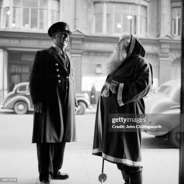Picture Post reporter Denzil Batchelor, in costume as Father Christmas, shares a joke with the doorman, at Harrods department store in London....