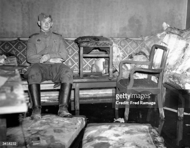 Russian soldier sitting on the sofa upon which German dictator Adolf Hitler is reported to have killed himself, in Hitler's shelter under the...