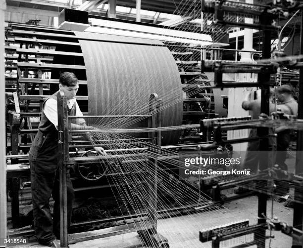 An employee operating a modern high speed creel in the warping department of the Wilson and Glenny Mill at Hawick in the Scottish Borders where tweed...