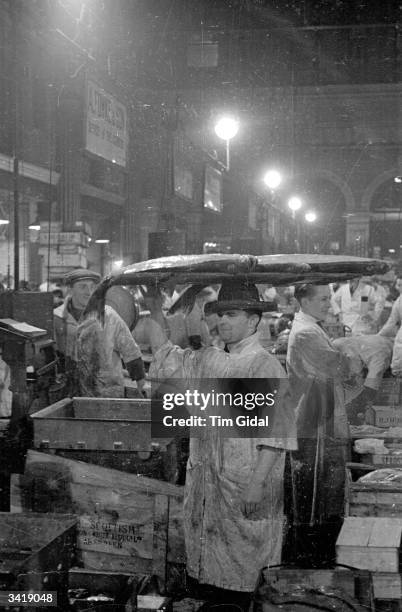 Porter carries a sample of Halibut from Aberdeen at Billingsgate fish market in London. Original Publication: Picture Post - 184 - Billingsgate -...