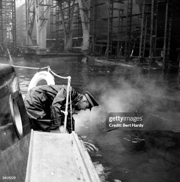 Member of the Scottish river police fishes something out of the water from his launch on the River Clyde. Clydeside is famous for its shipbuilding...