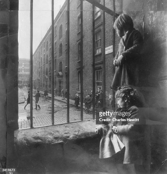 Two young children watching others play outside in Christmas street off Old Kent Road in South East London. Original Publication: Picture Post - 4277...