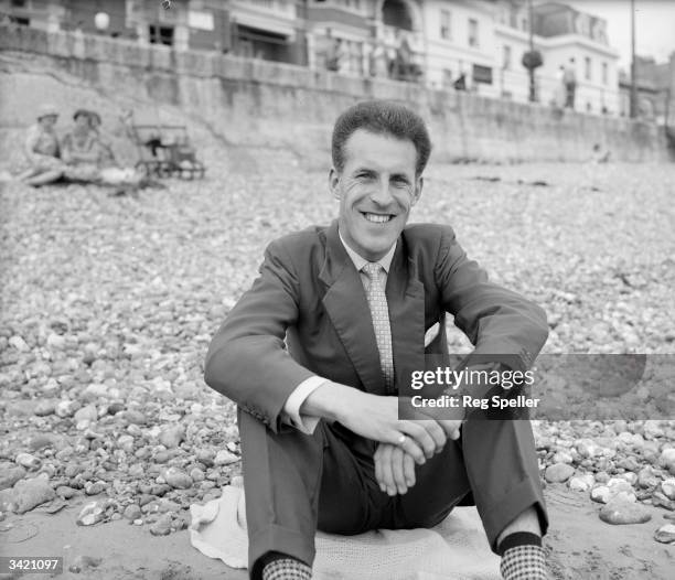 British entertainer and television presenter Bruce Forsyth sitting on a beach.