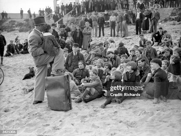 Crowd of holiday-makers on the beach at Porthcawl, Mid Glamorgan, Wales, watching a performance by a ventriloquist and his doll.