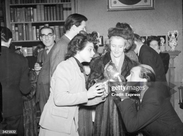 John Mills draining a punch bowl, assisted by his wife Mary Hayley Bell and Mary Morris, at a party for the cast of 'Duet For Two Hands'.
