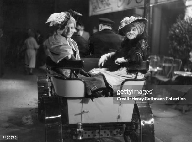 Two actresses riding in a car from 1900 in the film 'The Girl From Maxim's', a period farce directed by Alexander Korda.