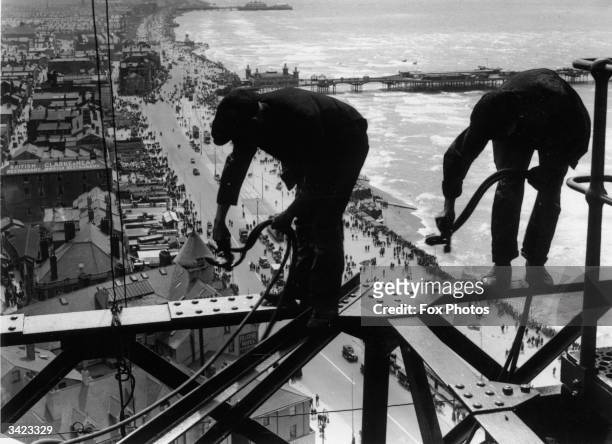 Balancing on girders high above the promenade workmen repair Blackpool Tower.