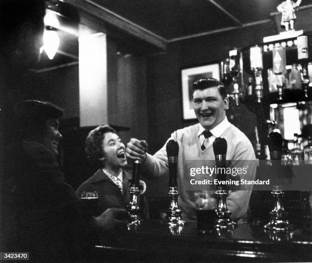 Customers in an East End pub, London enjoying a joke with the landlord as he pulls a pint.