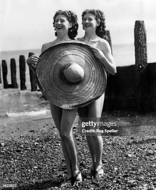 Twin sisters Doris and Edith Evanson holding up a large sombrero to shield their bodies on Worthing beach.